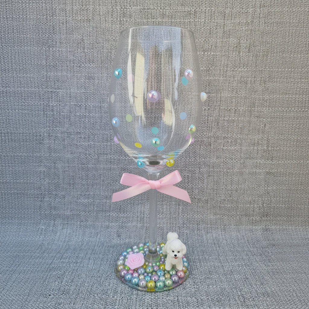 Decorative wine glass with colorful beads and a small figurine on a textured surface