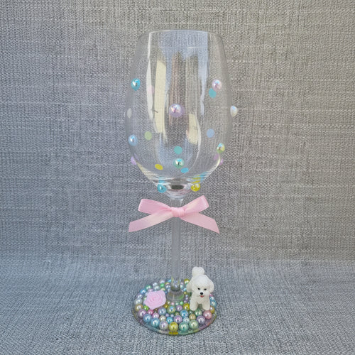 Decorative wine glass with colorful beads and a small figurine on a textured surface