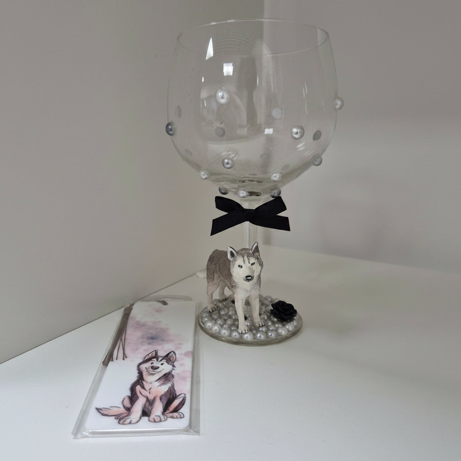 Decorative wine glass with a dog figurine and bow, accompanied by a matching bookmark on a white surface.