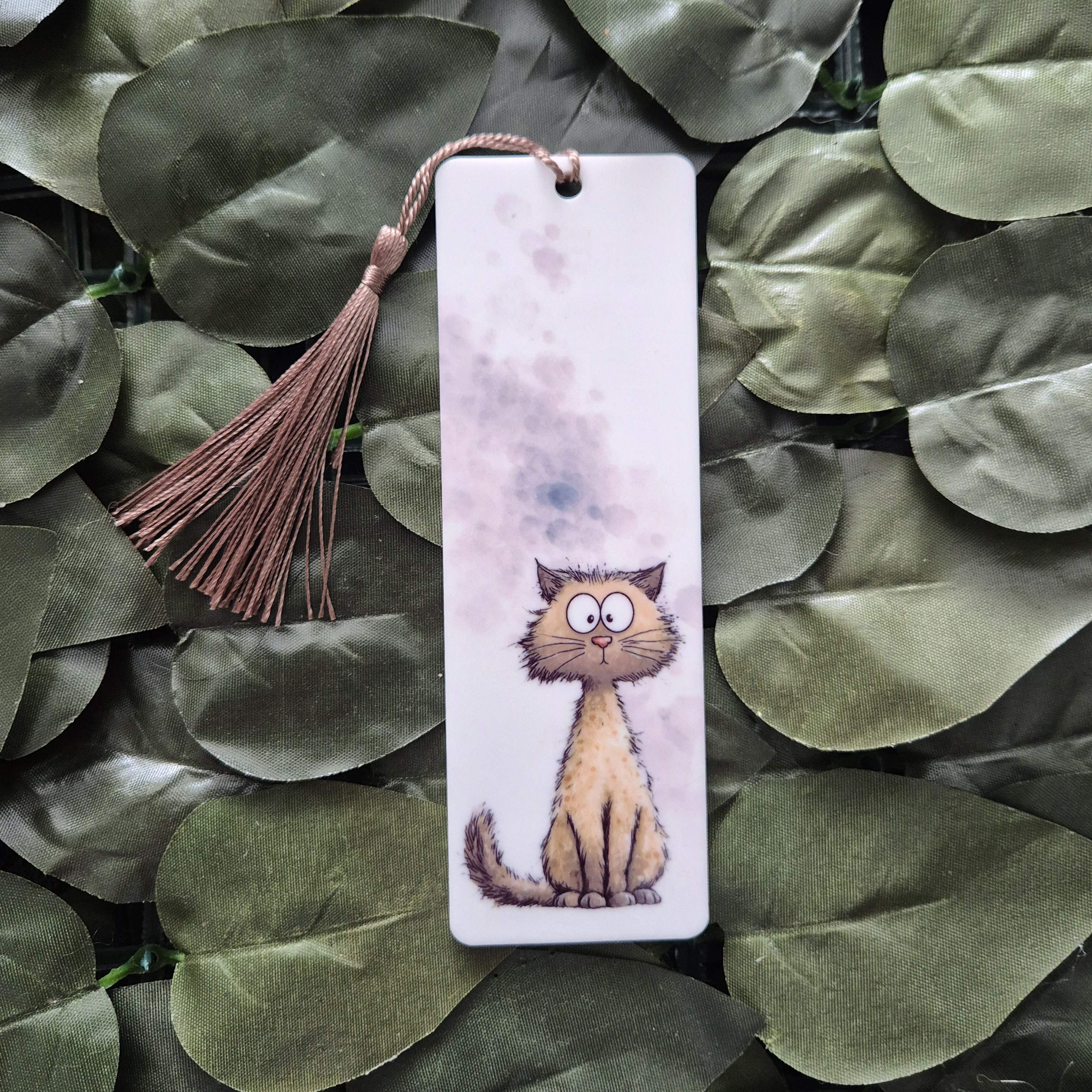 Bookmark with a cat illustration and  tassel on green leaves