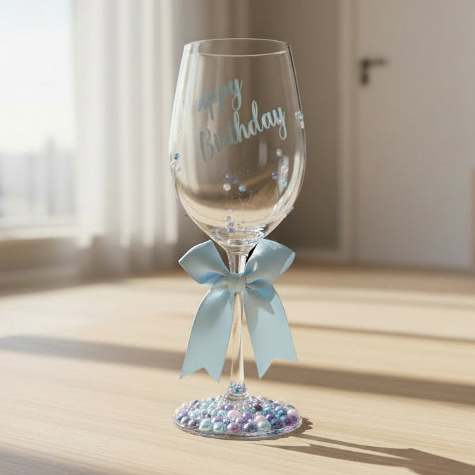 Decorative wine glass with 'Happy Birthday' text, blue bow, and bead embellishments.