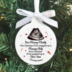 A round white Christmas ornament with a white ribbon bow, featuring a black ultrasound image and a personalized message for 'Mummy & Daddy' about being snuggled up in 'Mummy's Belly' and 'Your Arms'. The ornament is displayed hanging against a green pine tree background.