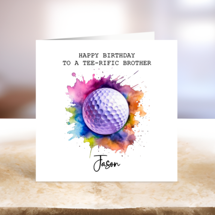 Greeting card with colorful watercolor design of a golf ball and text 'Happy Birthday to a tee-rific brother Jason' on a marble surface.