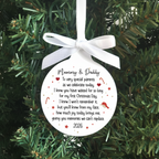 A round white Christmas ornament with a white ribbon bow, featuring a printed sentimental message for 'Mummy & Daddy' with small red hearts and stars, hanging against a green pine tree background.