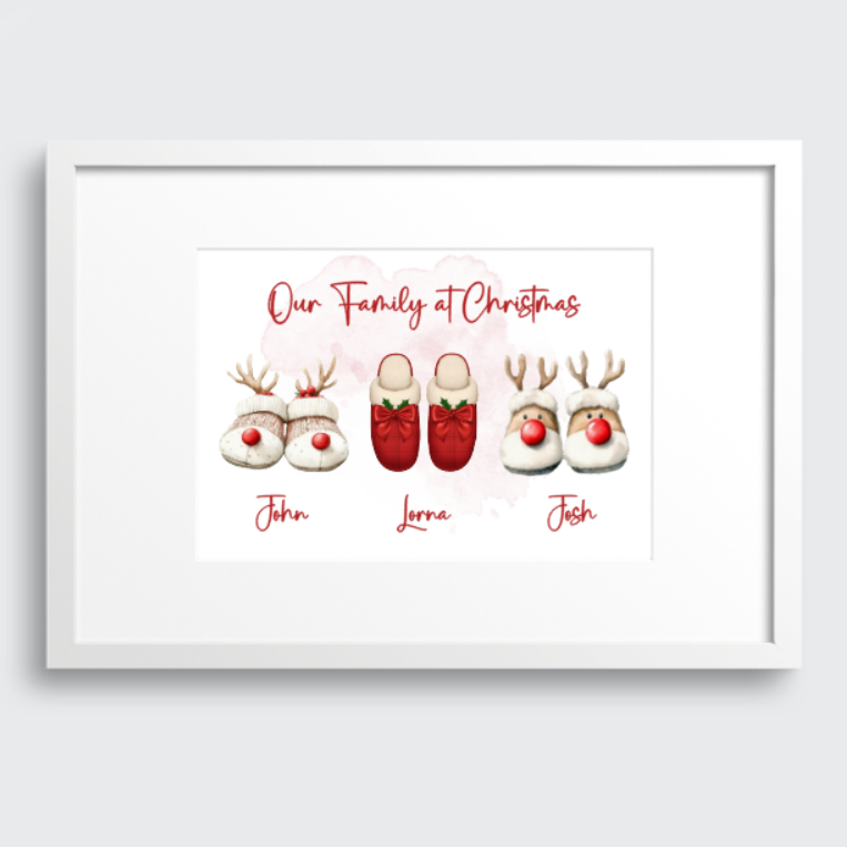 A framed personalized Christmas print featuring watercolor-style reindeer slippers with names underneath, shown against a light gray background.