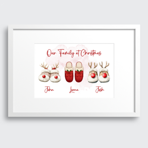A framed personalized Christmas print featuring watercolor-style reindeer slippers with names underneath, shown against a light gray background.